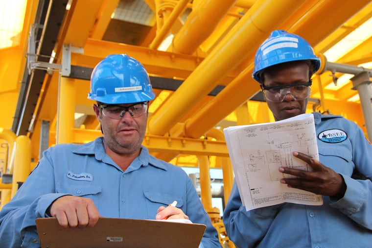 Offshore crew in hard hats reviewing drawings on an offshore production facility